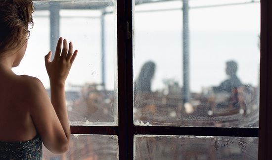 Fotografía de una mujer que mira a través de una ventana a una pareja conversando en una cafetería